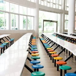Clean school cafeteria with many empty seats and tables.